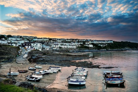Boats in a small harbour at low tide, with a village in the background and a moody sunset