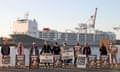 Animal welfare protesters are seen at a rally in front of the Al Kuwait live export ship as sheep are loaded in Fremantle harbour, Tuesday, June 16, 2020. A number of crew members tested positive with COVID-19 and quarantined when the ship arrived in Fremantle over three weeks ago. They were scheduled to pick up the sheep for transport to the Middle East before the northern summer ban on June 1st came into place to stop sheep dying from heat stress. The Federal Department of Agriculture have now approved a second application to transport the sheep and it must leave by Wednesday.(AAP Image/Richard Wainwright) NO ARCHIVING