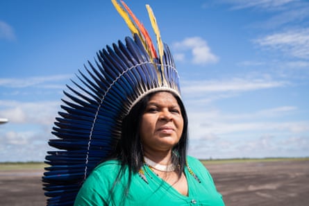 A woman in an elaborate feather headdress stands for a portrait.