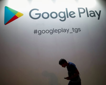 A man hunched over a smartphone stands in front of the Google Play logo
