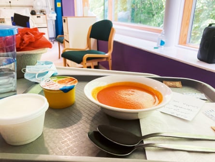 A bowl of tomato soup on a table over a hospital bed, alongside a carton of orange juice