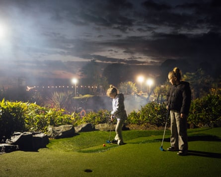 Two girls playing crazy golf on a spotlit course at night.
