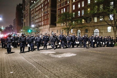 a large group police in helmets walk down a street in a color photo