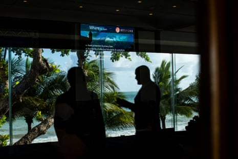 Silhouettes of two people with a presentation screen above them, palm trees and the beach seen through the window