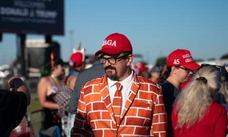 A man in a brick-pattern suit with a Maga hat outside with other Trump supporters.