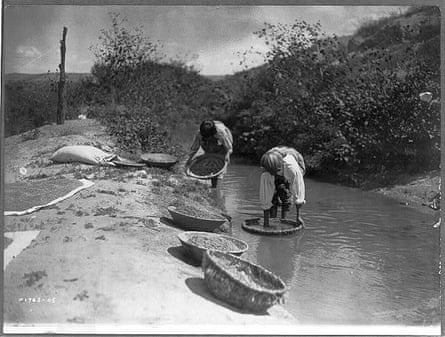 A 1905 photograph shows people dipping baskets of wheat into an acequia to dissolve dirt and float away debris from the wheat kernels in the pueblo of San Juan, New Mexico.
