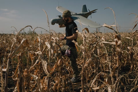 A soldier holds a plane-shaped drone on his soldier while standing in a cornfield
