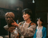 A woman works on a clay bust while another woman watches in the background.