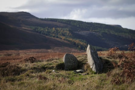 Rocks and stones on high moorland with bracken in the background, looking towards dark, looming hillsides under a grey sky.