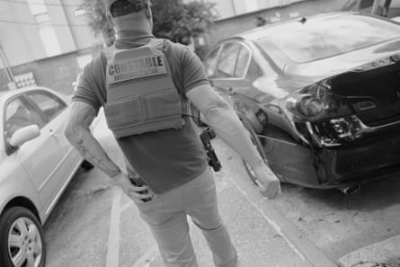 A man in a police vest walks through a parking lot