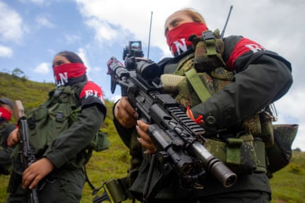 Fighters wearing green uniforms and red scarves over their faces holding large guns