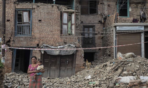 A woman carrying a child stands in front of damaged buildings in Patan, Nepal