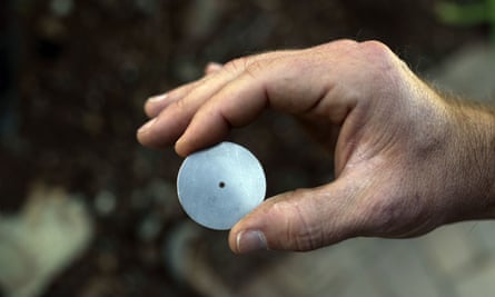 A person holding a tiny metal disc with a small hole in the center