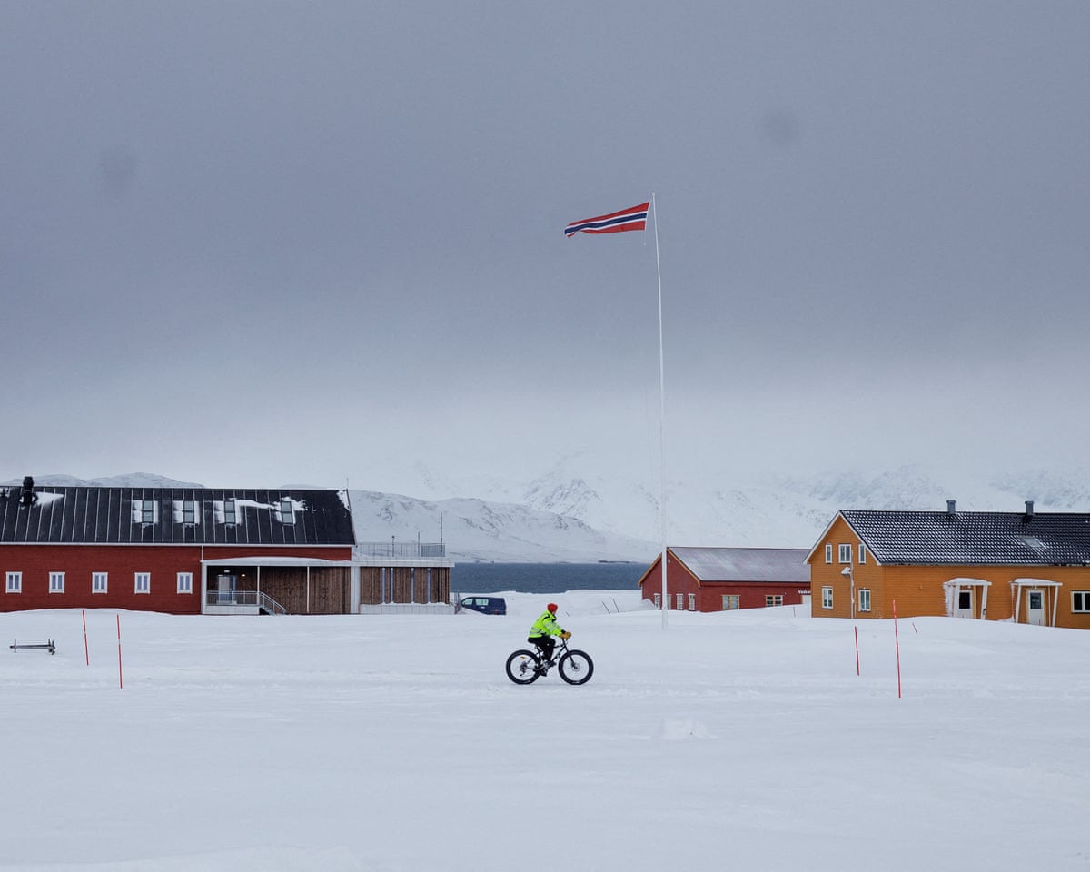 A resident rides a bike next to a Norwegian flag fluttering in the wind in Ny-Alesund, Svalbard, Norway.