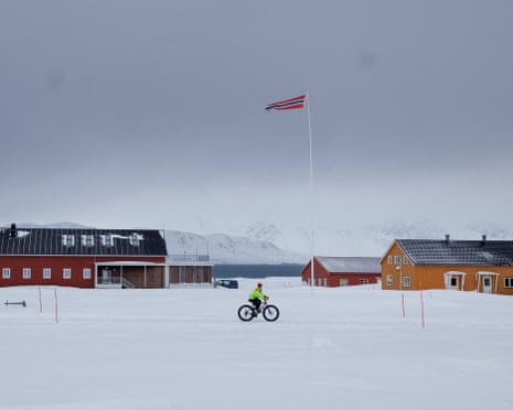 A resident rides a bike next to a Norwegian flag fluttering in the wind in Ny-Alesund, Svalbard, Norway.
