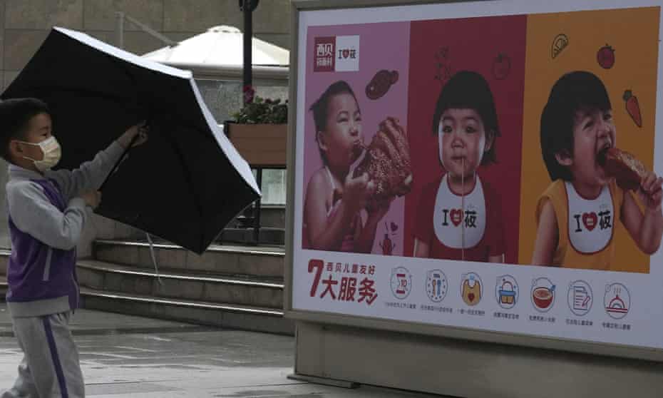 A child opens an umbrella near an advertisement for a restaurant featuring young children in Beijing on Monday.