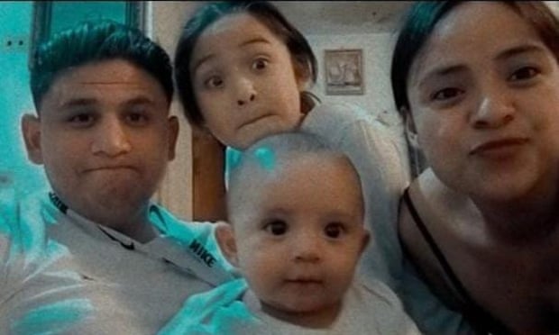 A man smiles in a picture with his wife and two young children.