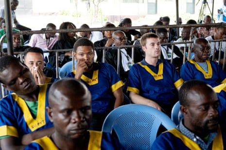 A room full of accused people sitting in matching blue and yellow uniforms.