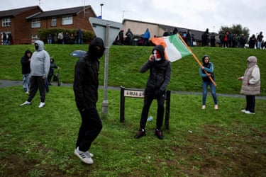 People gather at Garvaghy Road, some wearing balaclavas, another with an Irish flag
