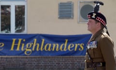 James Roddis standing in army uniform in profile in front of a banner which reads 'Welcome Home the Highlanders'