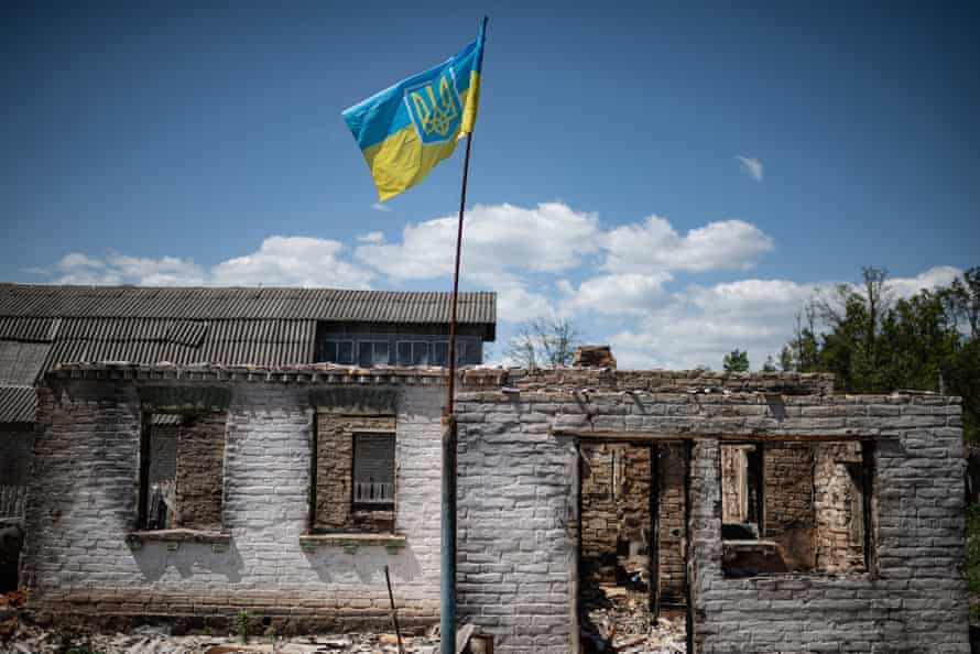 A Ukrainian national flag with a coat of arms is seen next to a burnt house in Moshchun, Ukraine.