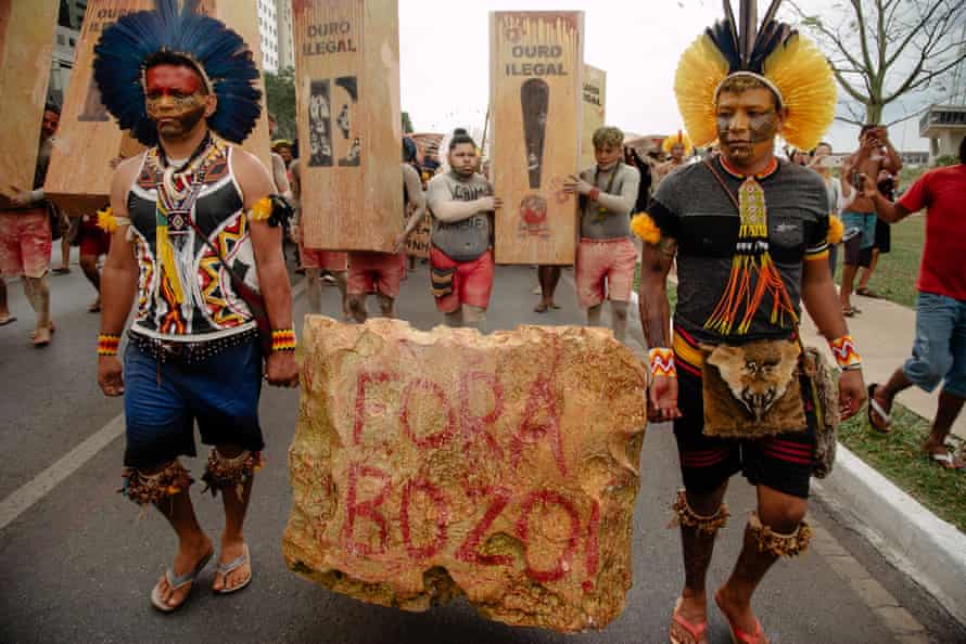 Hitup and Wekanã Pataxó carry a stone that represents a gold nugget during an act in Brasília. The nugget is painted in red with the saying “Fora Bozo” which means Out Bolsonaro.