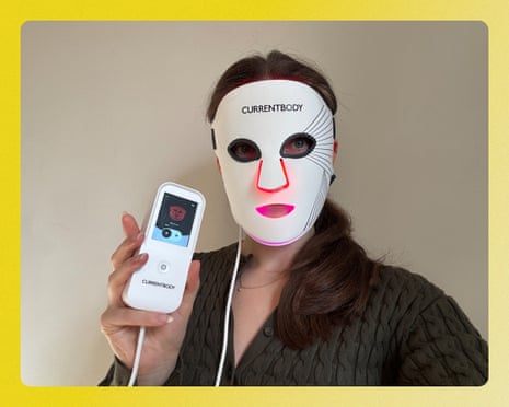 A woman wears a white LED face mask while holding its lit controller device