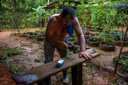 A man steadies a plank of wood on top of two wooden legs to hammer in a nail.