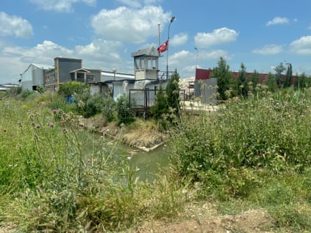 A recycling facility beside a waterway with green shrubs in the foreground