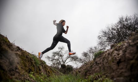 Woman in running shoes jumping across a small gap in the countryside