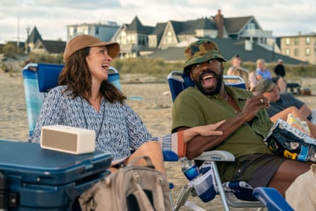 man and woman laugh while sitting in chairs at the beach