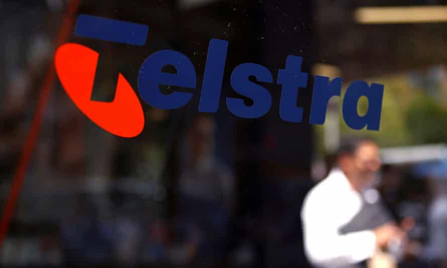 A man looks at his phone as he walks past a Telstra phone booth