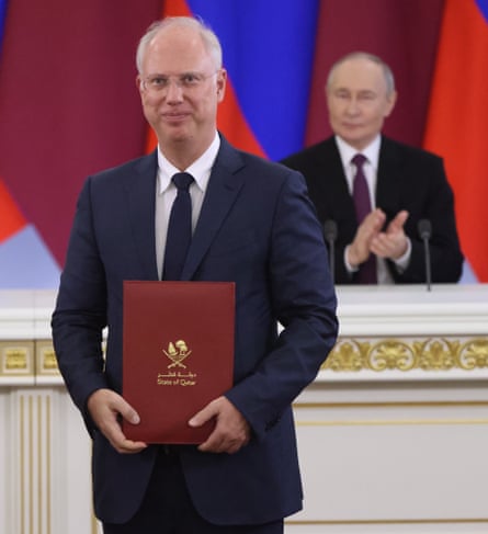 Dmitriev holds a folder and smiles at the camera as Putin applauds in the background