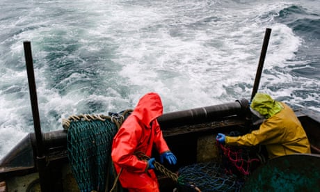 Two men in oilskins pulling on fishing nets at the back of a boat