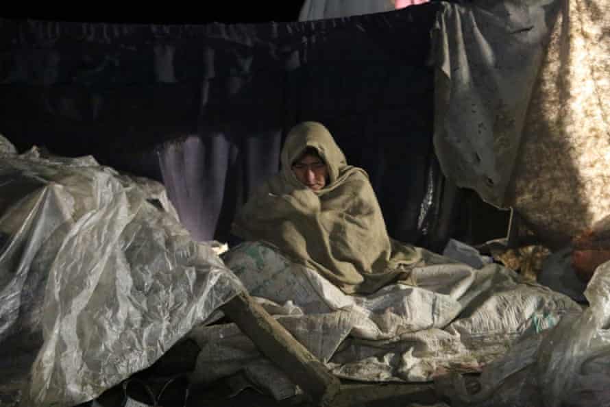 Een vrouw in de provincie Paktika die door de aardbeving dakloos is geworden, probeert warm te blijven.