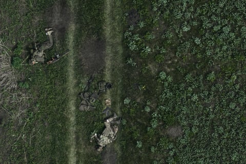 An aerial view shows the bodies of two Russian troops laying on a grassy landscape, with military equipment abandoned the ground between them
