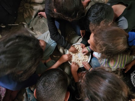 Overhead view of children sitting around a metal bowl and reaching into it for small pieces of bread