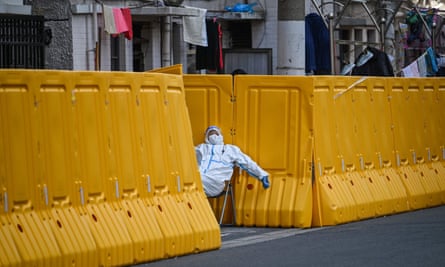 A worker in protective gear, guards the entrance to a neighborhood in Shanghai.