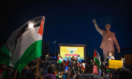 A crowd holds Palestinian flags under a statue of Nelson Mandela and a screen that reads 'Thank you South Africa'