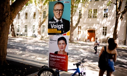 Campaign posters for the Christian Democratic Union candidate Mario Voigt and the Sahra Wagenknecht Alliance on a pole on a sunny street with people standing or walking nearby