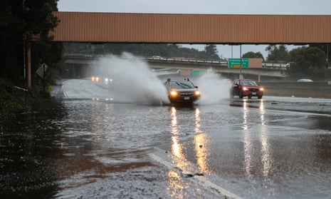 A car sends up two sprays of water as it drives on a flooded highway.
