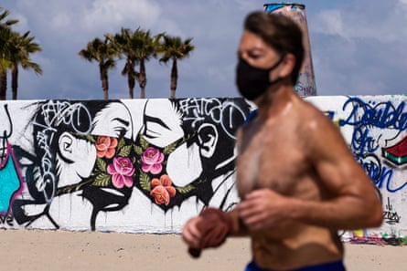 A man jogs past a mural showing a couple kissing with face masks next to the beach in Venice, Los Angeles county.