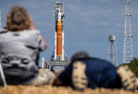 People out of focus in the foreground, with the rocket in focus in the distance on its launchpad