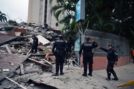 Municipal police officers stand next to the remains of a collapsed structure following an earthquake
