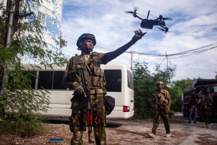 A black soldier in combat gear and holding an assault rifle launches a small observational drone as another soldier look on