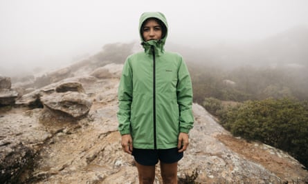 A woman, zipped up in a hooded Patagonia jacket, stands on a rock in front of fog on mountains