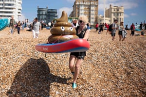 A woman smiles as she carries an inflatable surfboard being ridden by an inflatable cartoon poo on to Brighton beach