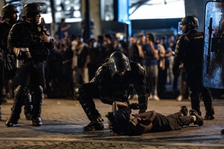 Riot police officers handcuff a supporter who is laid on the ground