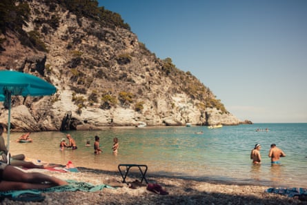People in the water off a beach with steep cliffs in the background