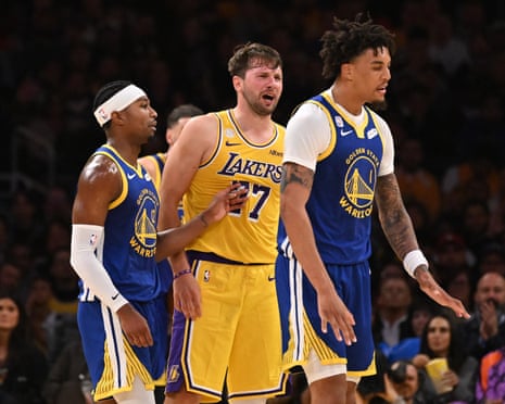 Luka Doncic reacts after a foul, flanked by two Warriors players on court